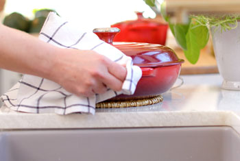a woman dries a cast iron braiser with a dish towel