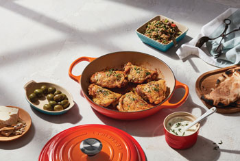 chicken in a flame orange braiser surrounded by sides and sauces