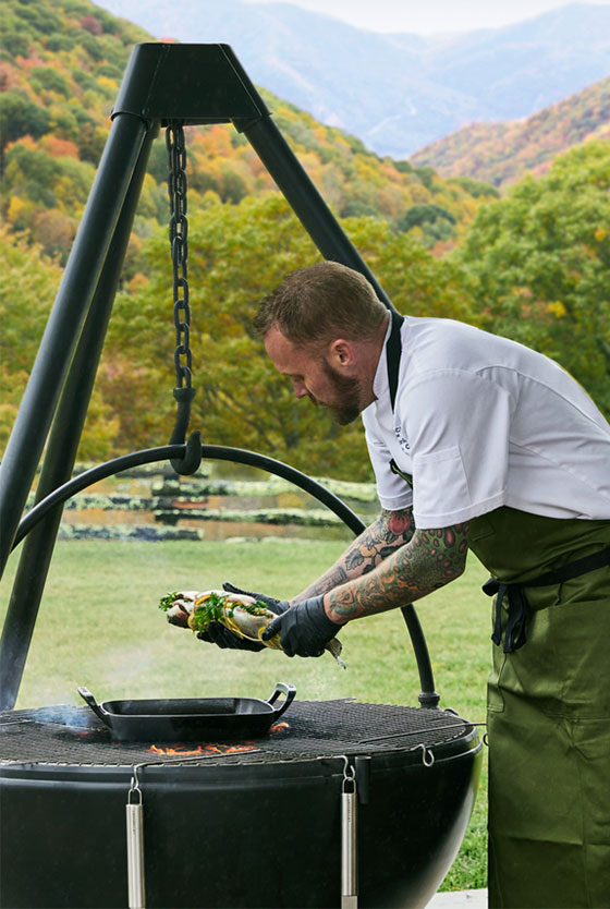 a chef prepares food with the alpine skillet over a large outdoor grill