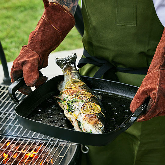 cooking fish in a black cast iron grill basket in an outdoor grill