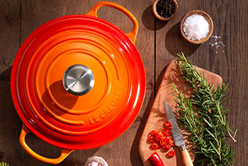 flame orange dutch oven next to herbs