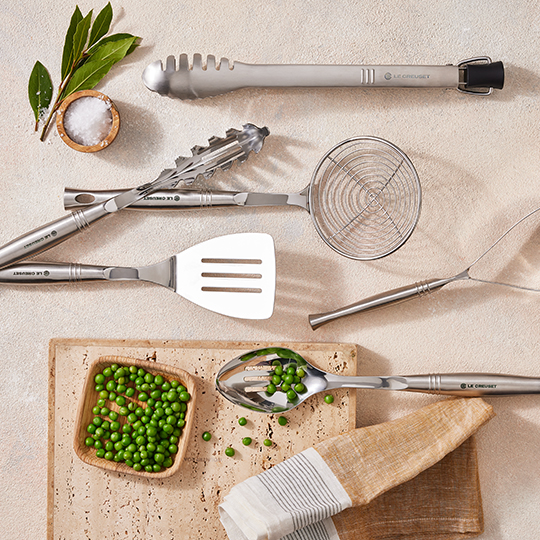Stainless steel tongs next to nonstick pan filled with asian noodles
